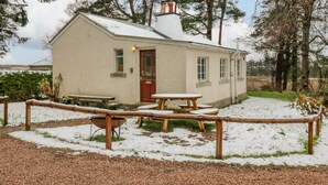 A small, single-story building with a red door and windows, surrounded by snow-covered ground and trees.