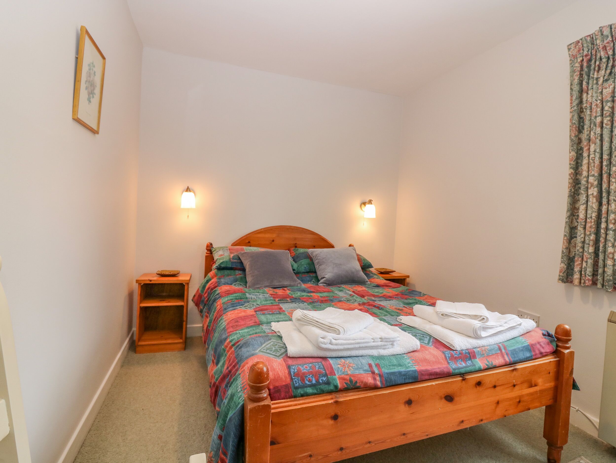 A neatly made bed with a colorful quilt, two bedside tables with lamps, and a small wooden nightstand.