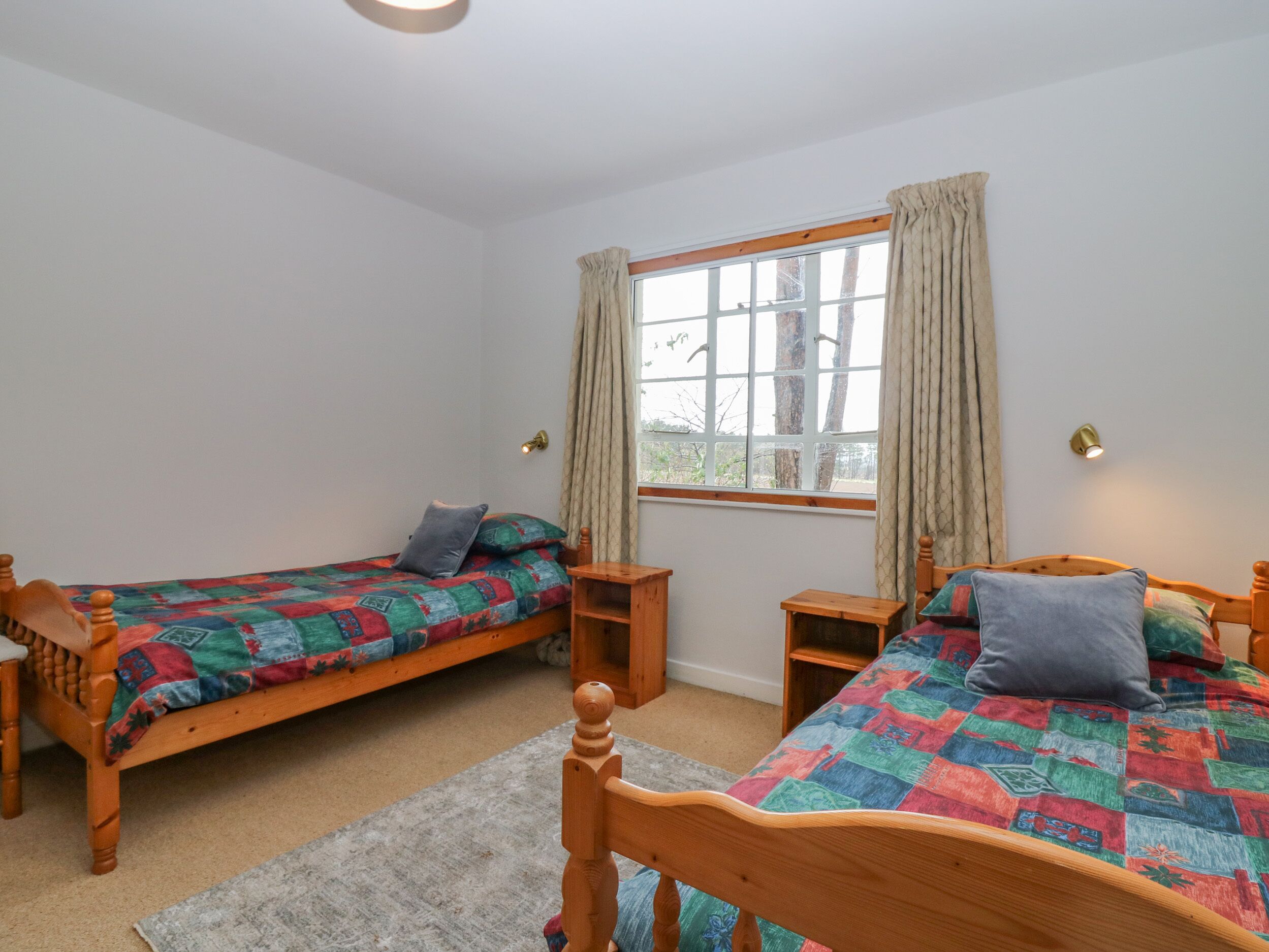 A bedroom with two wooden beds, a window with curtains, and a nightstand.