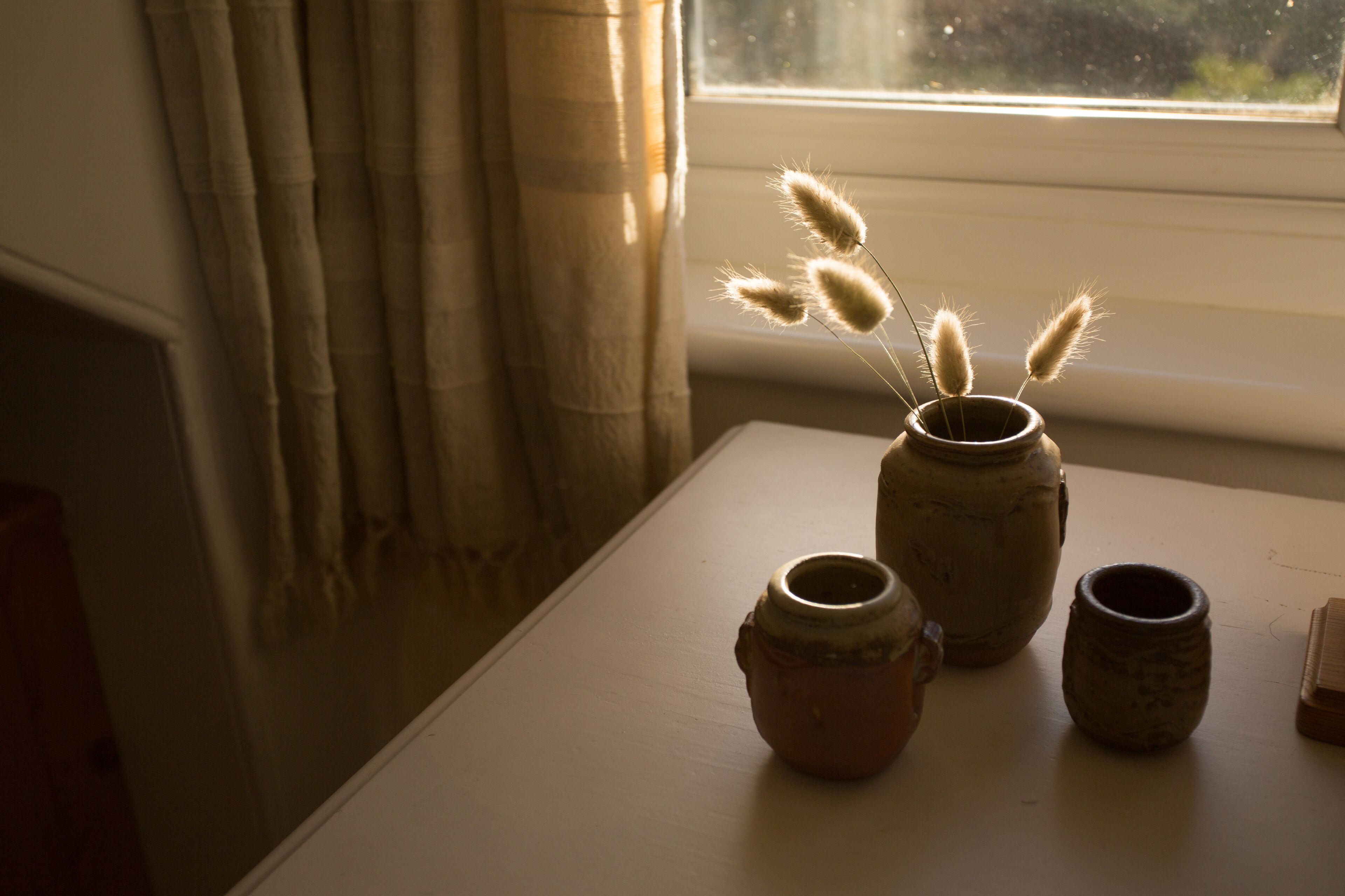 A table with three ceramic pots and a window with curtains.