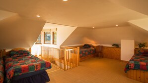 A cozy attic bedroom with two beds, a wooden railing, and a view of the outdoors through a window. - The White Cottage (Elgin)