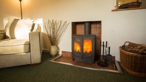 A cozy living room with a sofa, a fireplace, a lamp, and a vase with branches. - The White Cottage (Elgin)