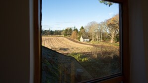 A view through a window of a rural landscape with a house, fields, and trees. - The White Cottage (Elgin)