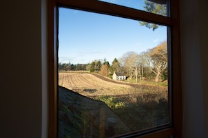 A view through a window of a rural landscape with a house, fields, and trees.