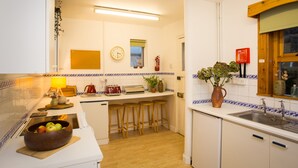 A kitchen with a wooden countertop, stools, a sink, a clock, and a fire extinguisher. - The White Cottage (Elgin)