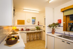 A kitchen with a wooden countertop, stools, a sink, a clock, and a fire extinguisher.