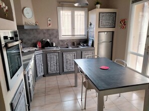 A compact kitchen with a dining table, a refrigerator, and a window with blinds. - FAMILY HOME WITH PRIVATE POOL SLEEPS 10 (Châteauneuf-du-Pape)