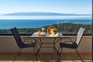 A dining table with chairs, breakfast items, and a view of the sea. - Sun Spalato Residence (Makarska)