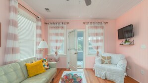 A living room with a sofa, a coffee table, a television mounted on the wall, and a door leading outside. - Clamdigger PETS  Ocean Block. Screened Porch (Tybee Island)