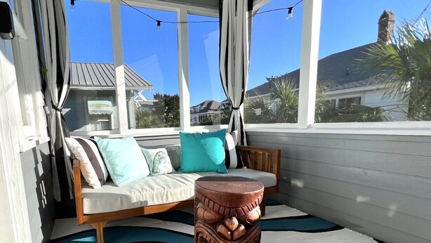 A covered porch with a wooden bench and a round wooden table, a patterned rug, and a view of houses in the background. - Clamdigger PETS  Ocean Block. Screened Porch (Tybee Island)