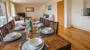 A dining area with a wooden table set for four, surrounded by chairs. There is a television on a stand against the wall, and a wooden door leading to another room. - Redwood, Retallack (St. Columb Major)