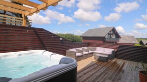A wooden deck with a hot tub, wicker furniture, and a view of a house in the background. - Redwood, Retallack (St. Columb Major)