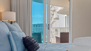 Une chambre d’hôtel avec un lit, une table de chevet, une lampe, une vue sur la ville et un balcon avec une balustrade.
