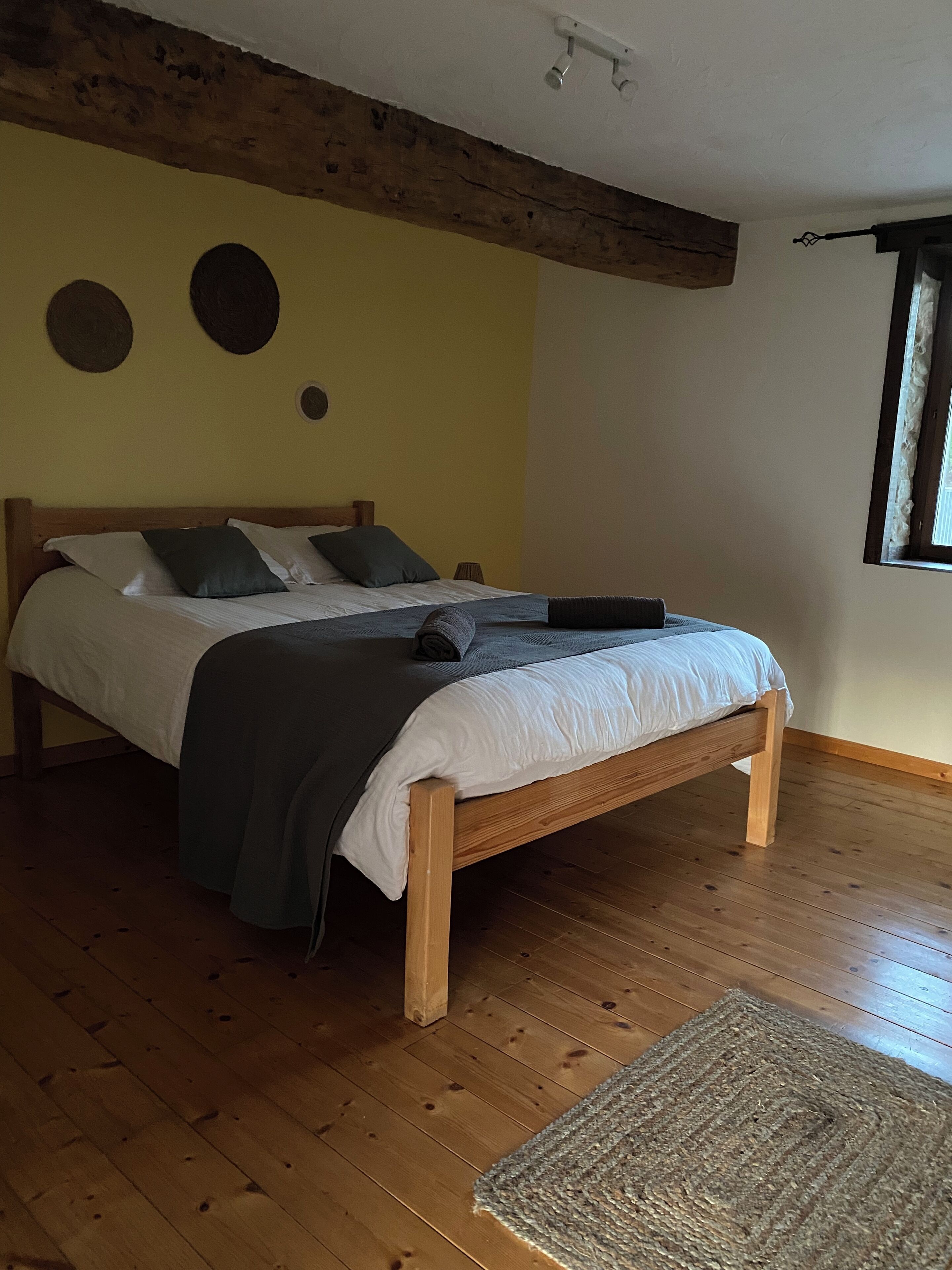 A bedroom with a wooden bed, a grey blanket, and a woven rug.