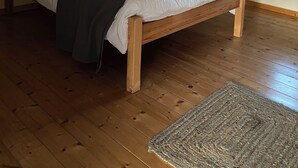 A bedroom with a wooden bed, a grey blanket, and a woven rug. - Gîte "La Longère", Domaine Métairie des Gâcheries, Dordogne/Périgord Vert (Champagne-et-Fontaine)