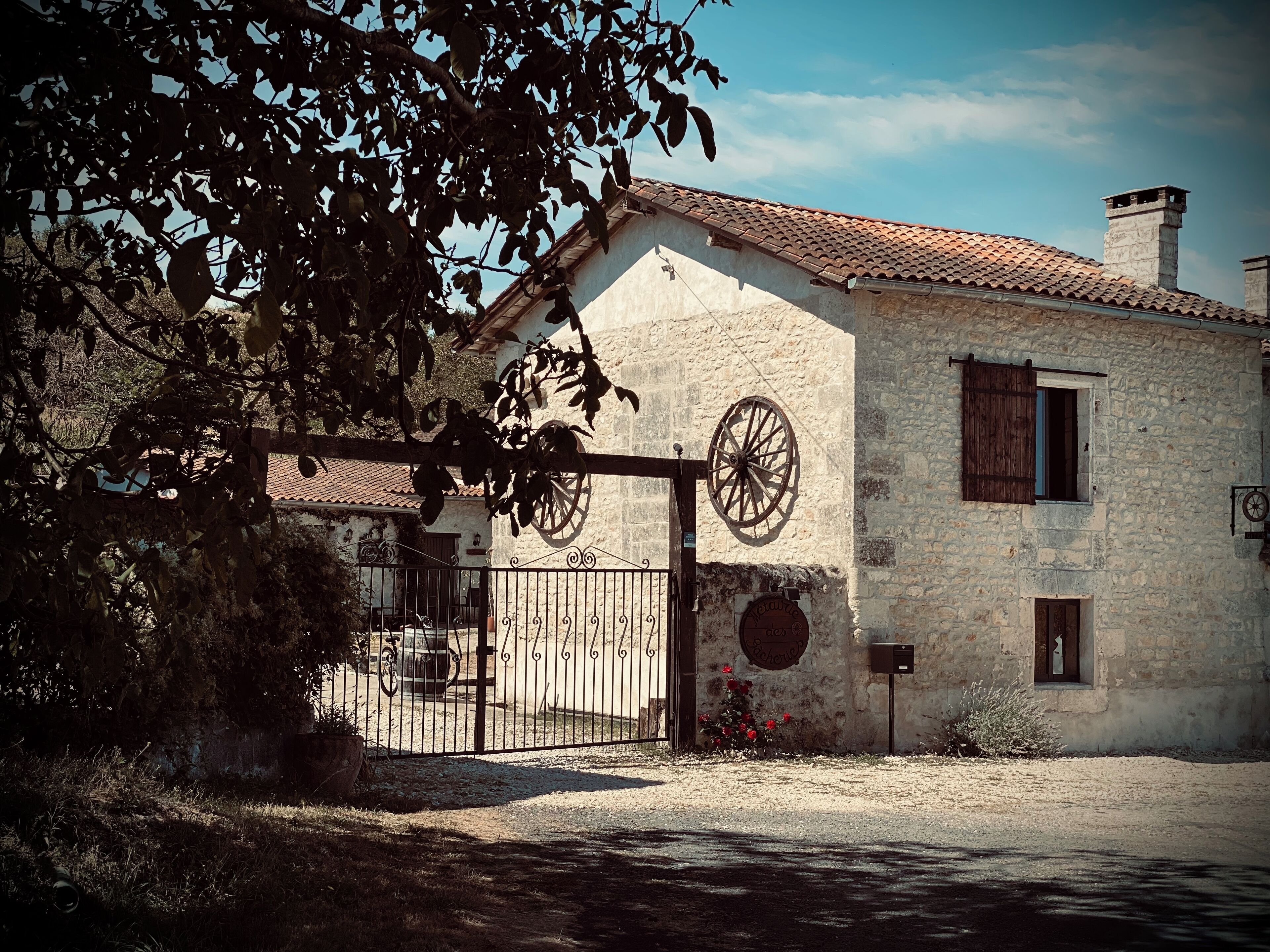 A rustic stone building with a traditional tiled roof, a large wooden wheel, and a gated entrance.