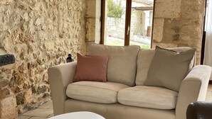 Un canapé beige avec deux coussins, une table blanche aux pieds en bois et un mur en pierre.