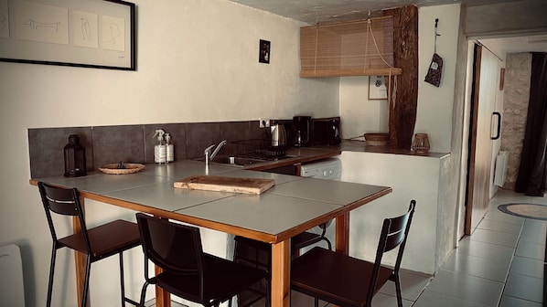 A compact kitchen with a central island, a sink, and a stove. There are four chairs around the island and a small window above the sink.