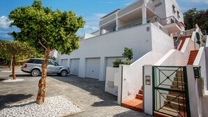 Edifici modern de color blanc amb un cotxe davant, un arbre i una entrada tancada per reixa.