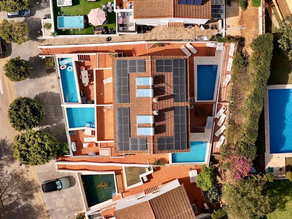 An aerial view of a hotel with multiple swimming pools, outdoor seating areas, and solar panels.