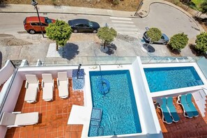 A rooftop swimming pool with lounge chairs and a clear view of the street below.