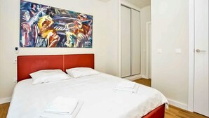 Habitació d'hotel amb un panell de fons vermell, un llit gran amb llençols blancs, un quadre a la paret i un armari amb portes corredisses.