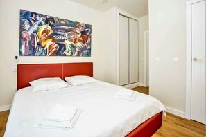 Une chambre d’hôtel avec une tête de lit rouge, un grand lit avec du linge de lit blanc, un tableau au mur et un placard à portes coulissantes.