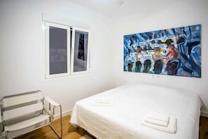 Ein Schlafzimmer mit Bett, Fenster, Gemälde und einem modernen Sessel.