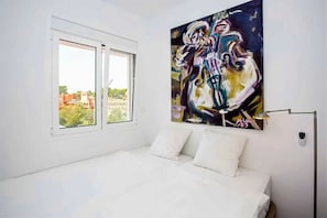A bedroom with a bed, a window, and a painting on the wall.