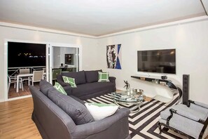 Ein modernes Wohnzimmer mit einer Couch, Sesseln, einem Couchtisch und einem Fernseher.