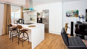 Une cuisine moderne avec des armoires blanches, un réfrigérateur en acier inoxydable et un four encastré. On y trouve deux tabourets de bar et un petit îlot central surmonté d’un tapis rond.