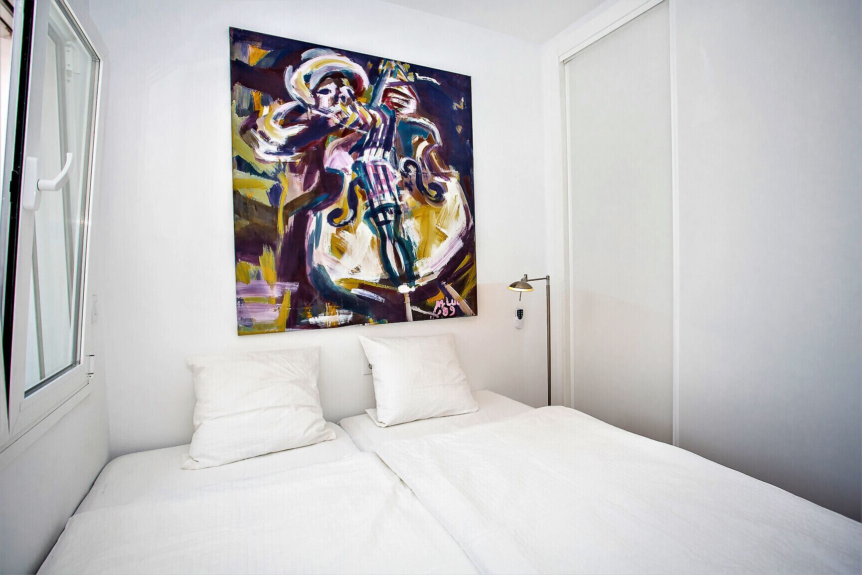 Une chambre à coucher avec un lit, des oreillers blancs, un tableau au mur et une porte.