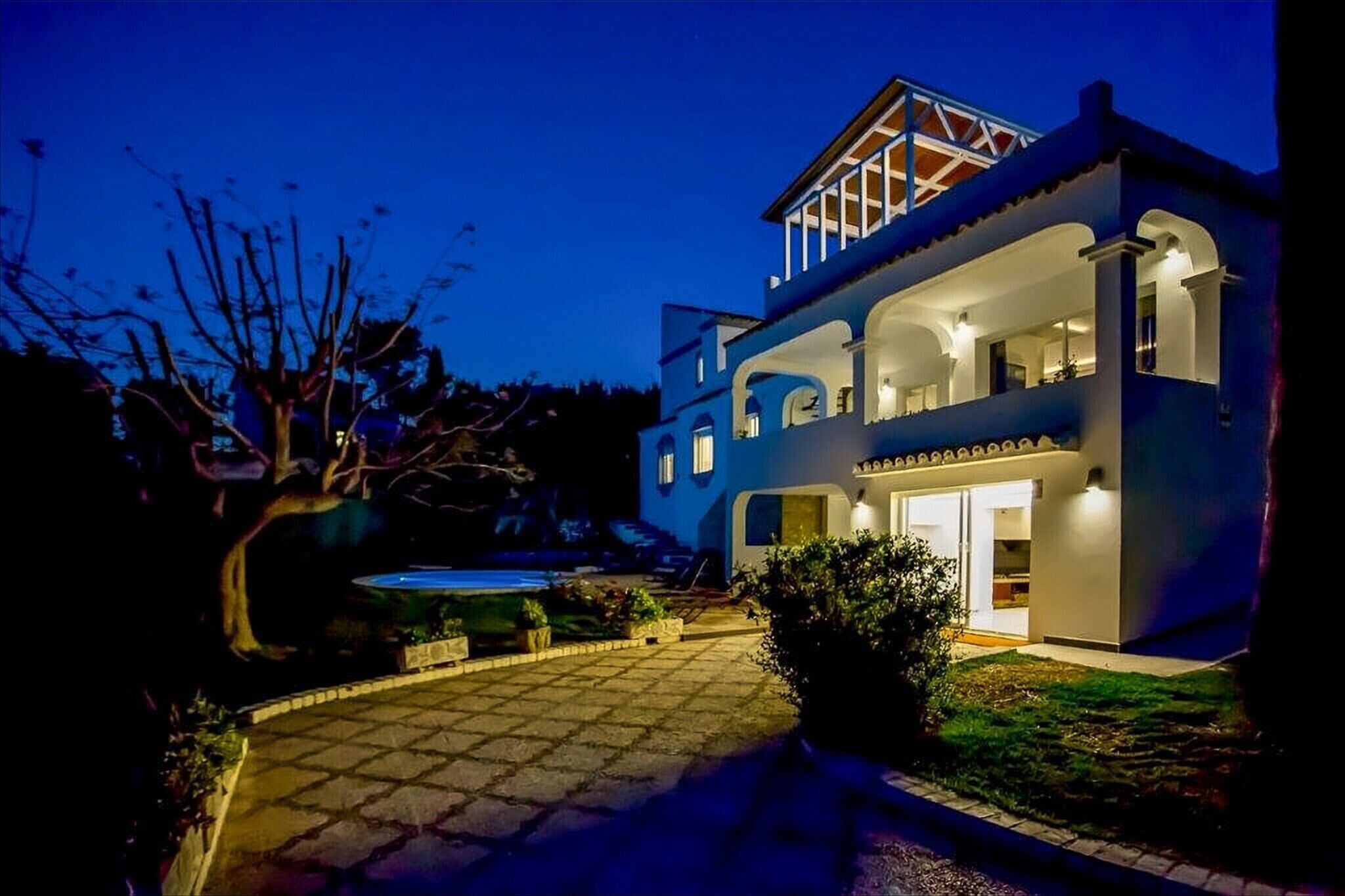 A two-story house with a balcony, a swimming pool, and a well-lit entrance.