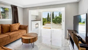 A modern living room with a sofa, a coffee table, a TV, and a sliding glass door leading to an outdoor area. - Villa with private swimming pool and jacuzzi Marbella (Mijas Costa)