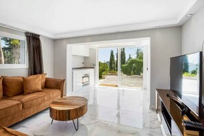 Una sala de estar moderna con un sofá, una mesa de centro, un televisor y un ventanal corredero que da a un área exterior.