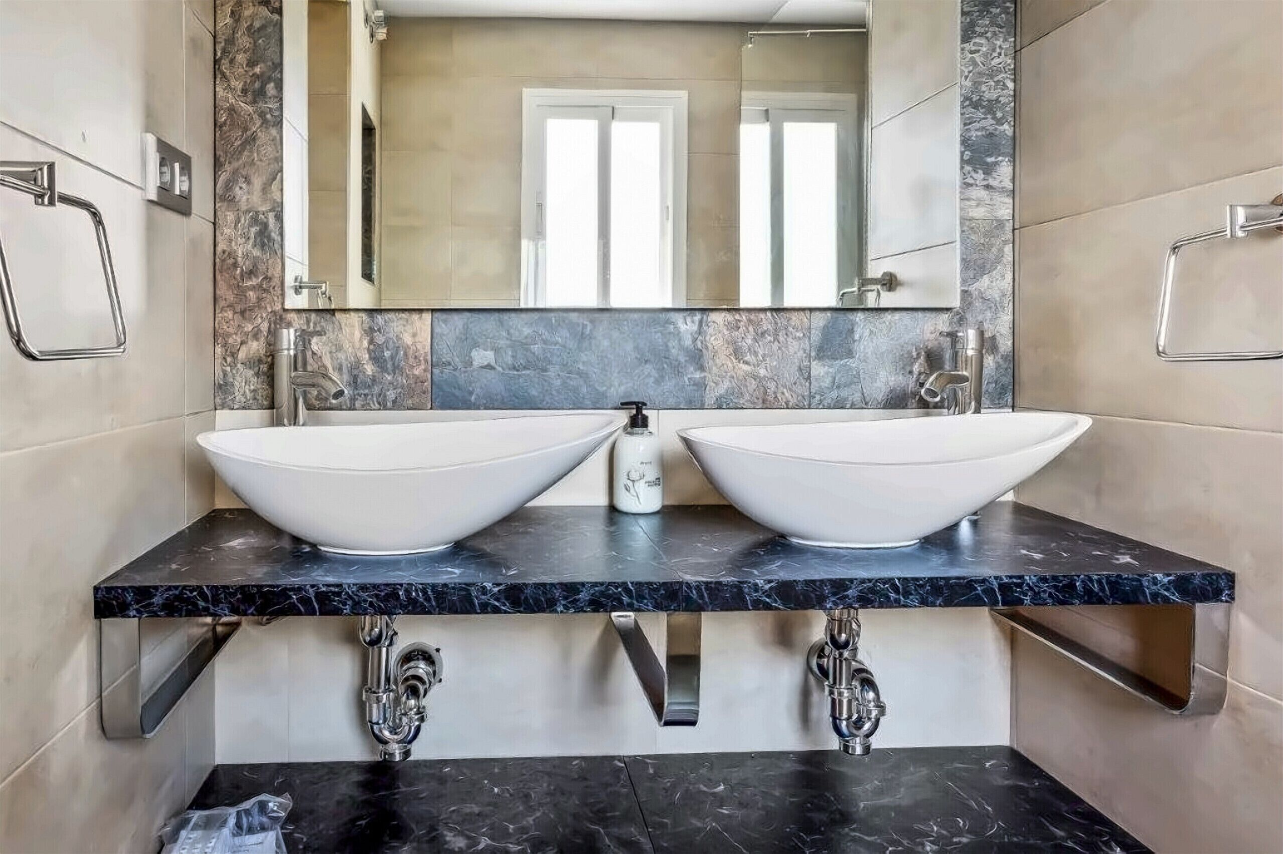 A bathroom with two large white sinks, a mirror above, and a marble countertop.
