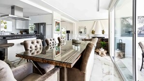 A modern kitchen with a large island, a dining area with leather chairs, and a view through large windows. - Villa with private swimming pool and jacuzzi Marbella (Mijas Costa)