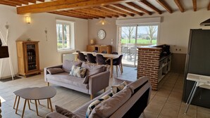 A cozy living room with a sofa, a dining table, and a kitchen area with a refrigerator and a brick oven.