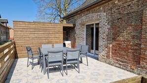 An outdoor patio with a wooden table and chairs, a brick wall, and a sliding glass door.