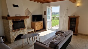 A living room with a stone fireplace, a television, a sofa, and a view of the outdoors.