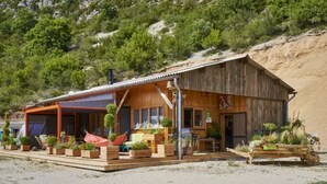 A rustic wooden building with a covered patio area, outdoor seating, and a garden.