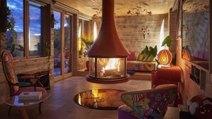 A cozy living room with a fireplace, comfortable seating, and large windows.