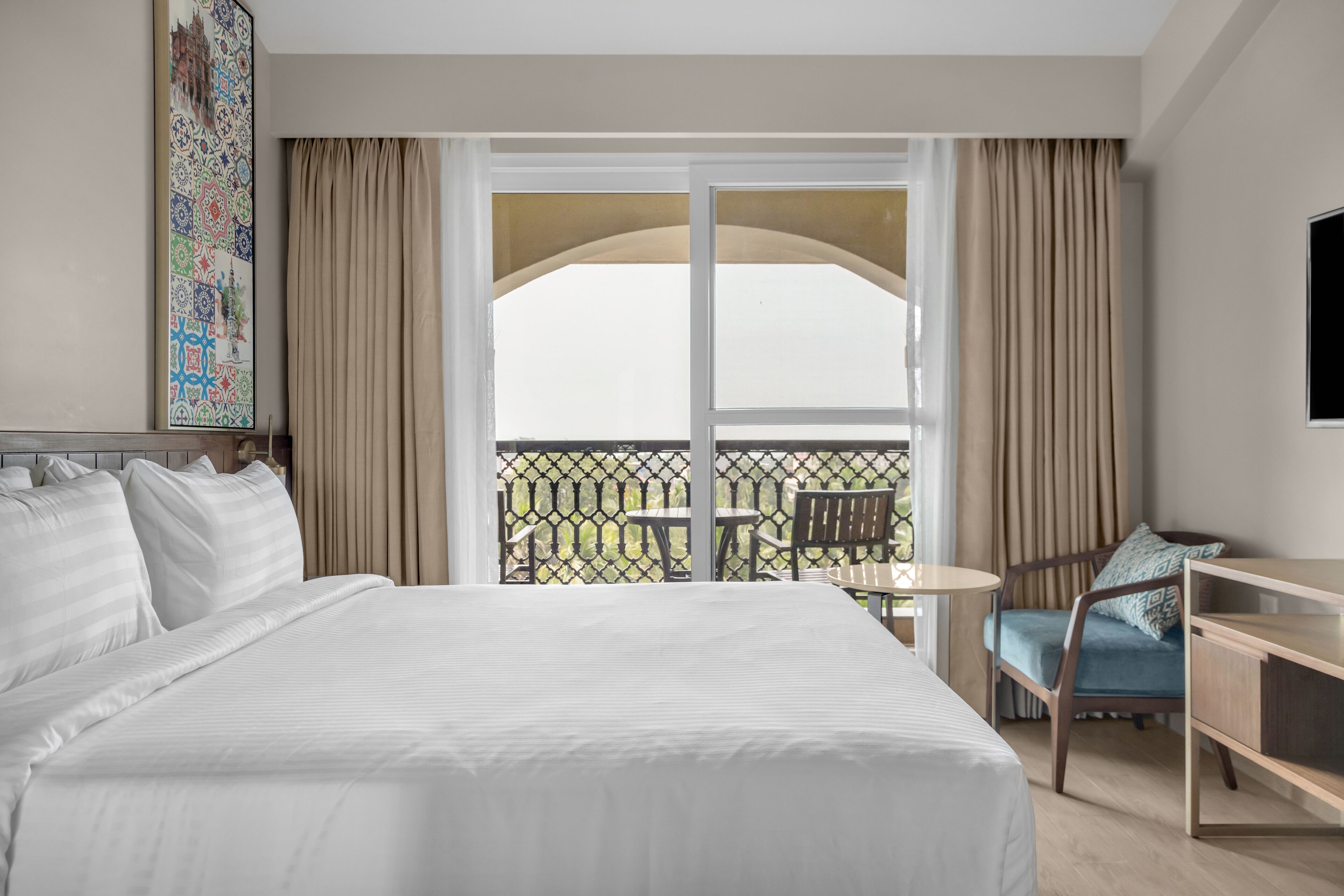 Habitación de hotel con una cama grande, un escritorio, una silla y un balcón con vistas.