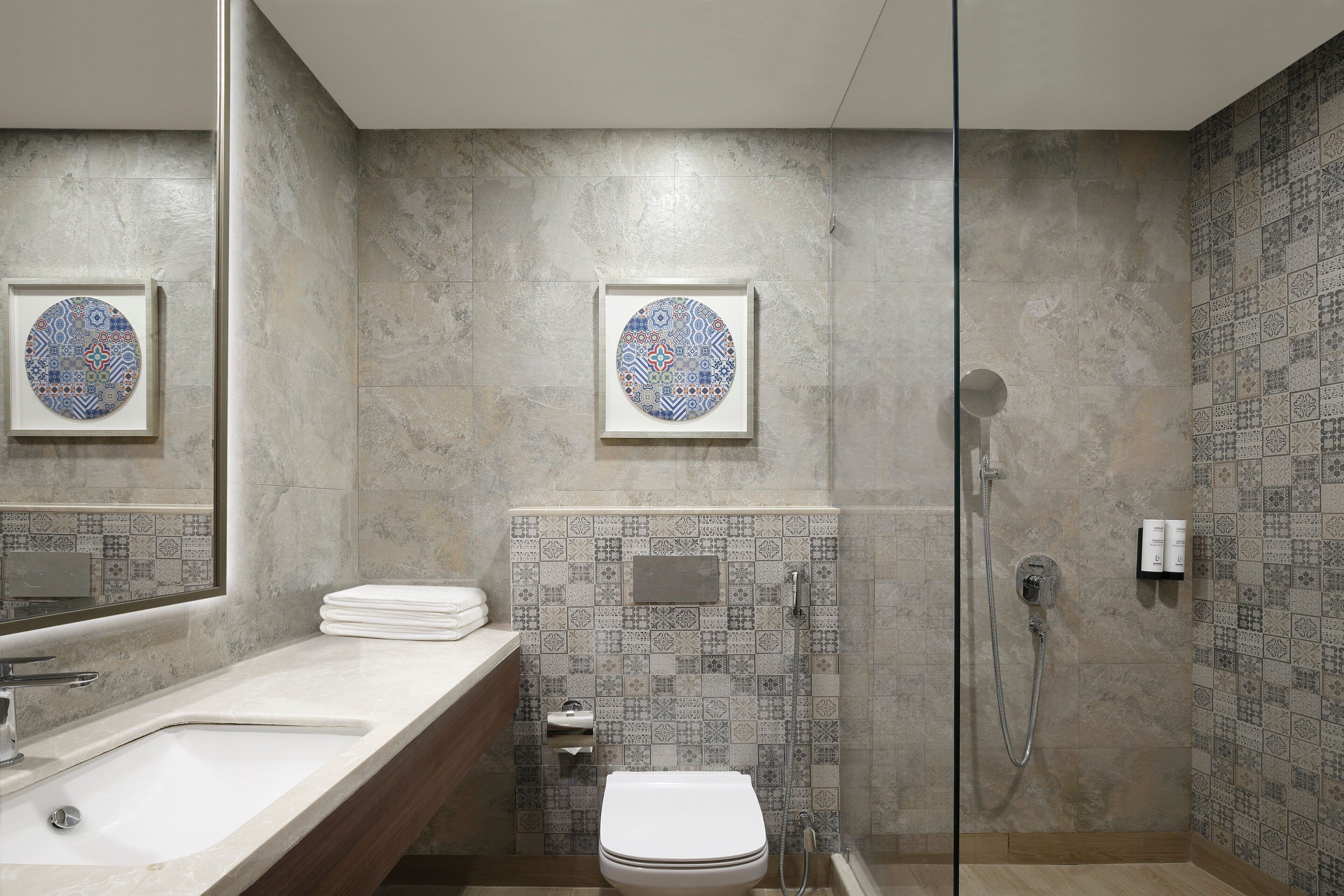 Un bagno con lavandino, servizi igienici e doccia. Presenta piastrelle decorate e opere d'arte incorniciate alle pareti.