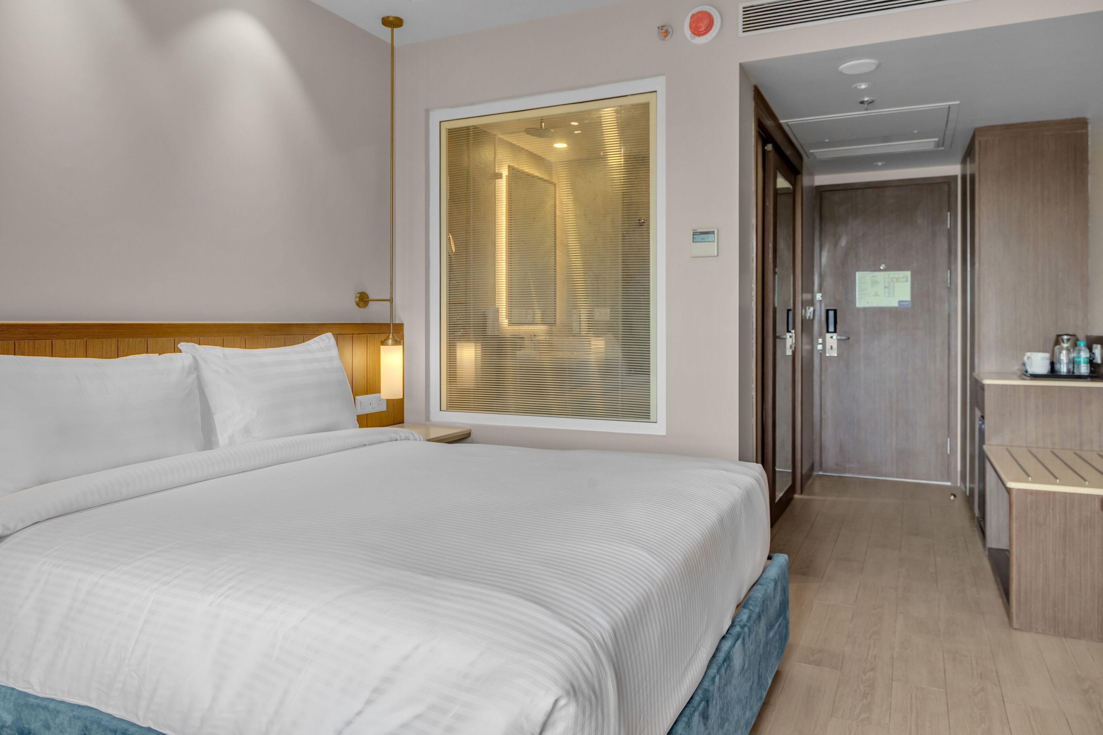 A hotel room with a large bed, a bedside table, a wardrobe, and a bathroom visible through a glass door.