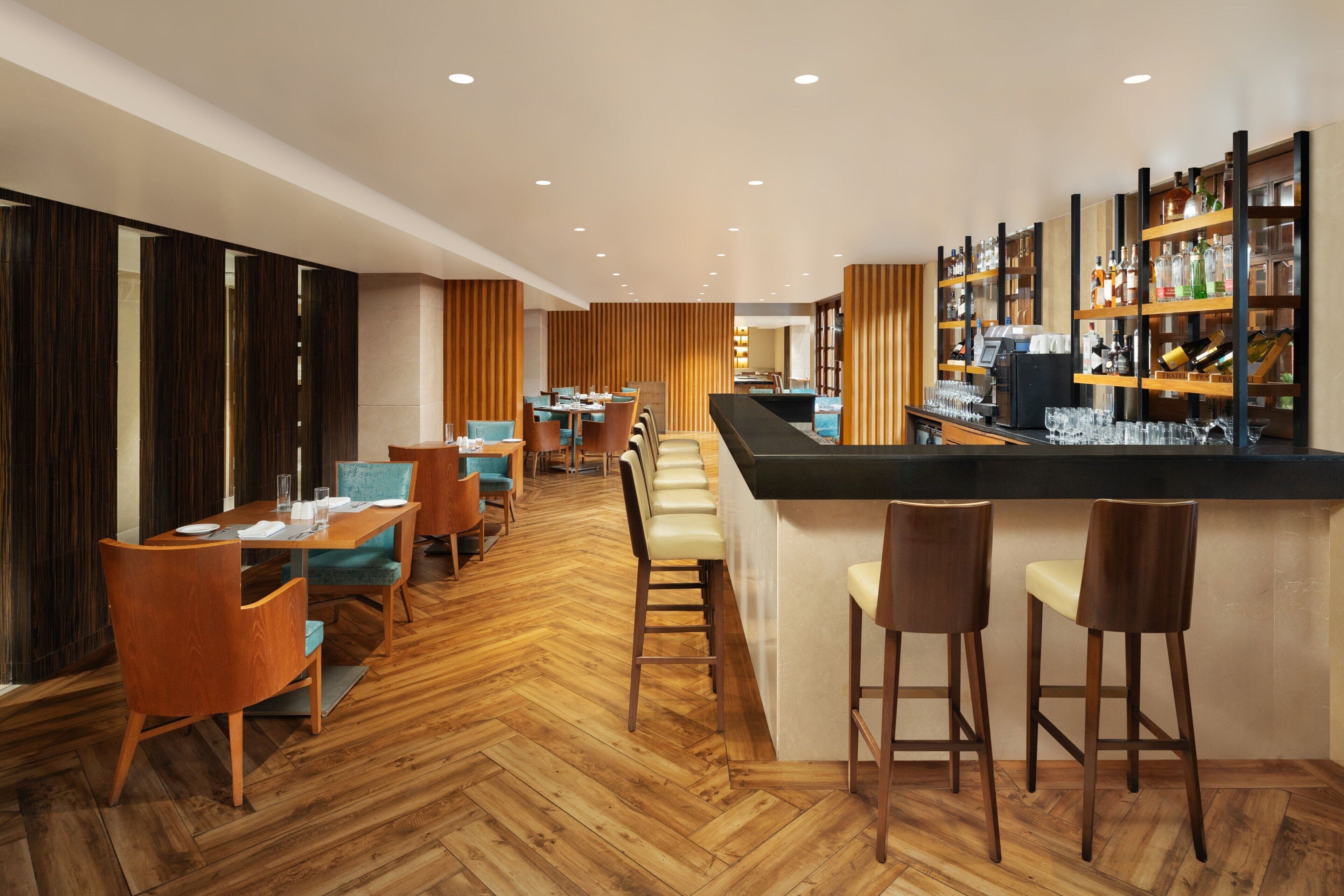 A modern bar area with wooden flooring, bar stools, and a counter with shelves of bottles.