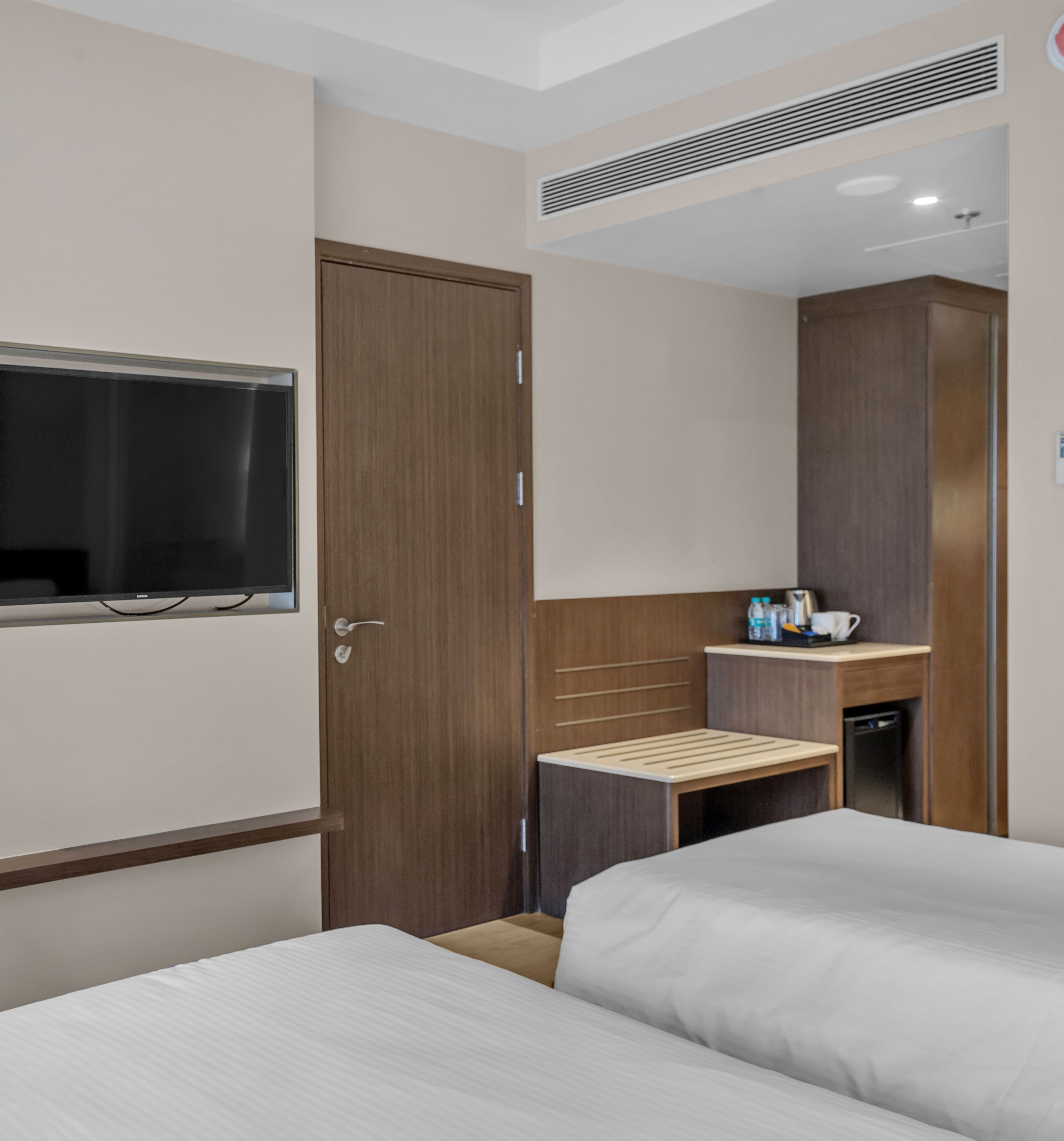 Habitación de hotel con dos camas, un armario de madera, un escritorio pequeño con espejo y un televisor montado en la pared.