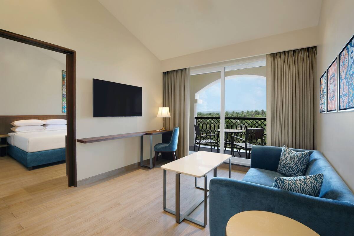Una habitación de hotel con cama, escritorio, sofá y balcón con mesa y sillas.