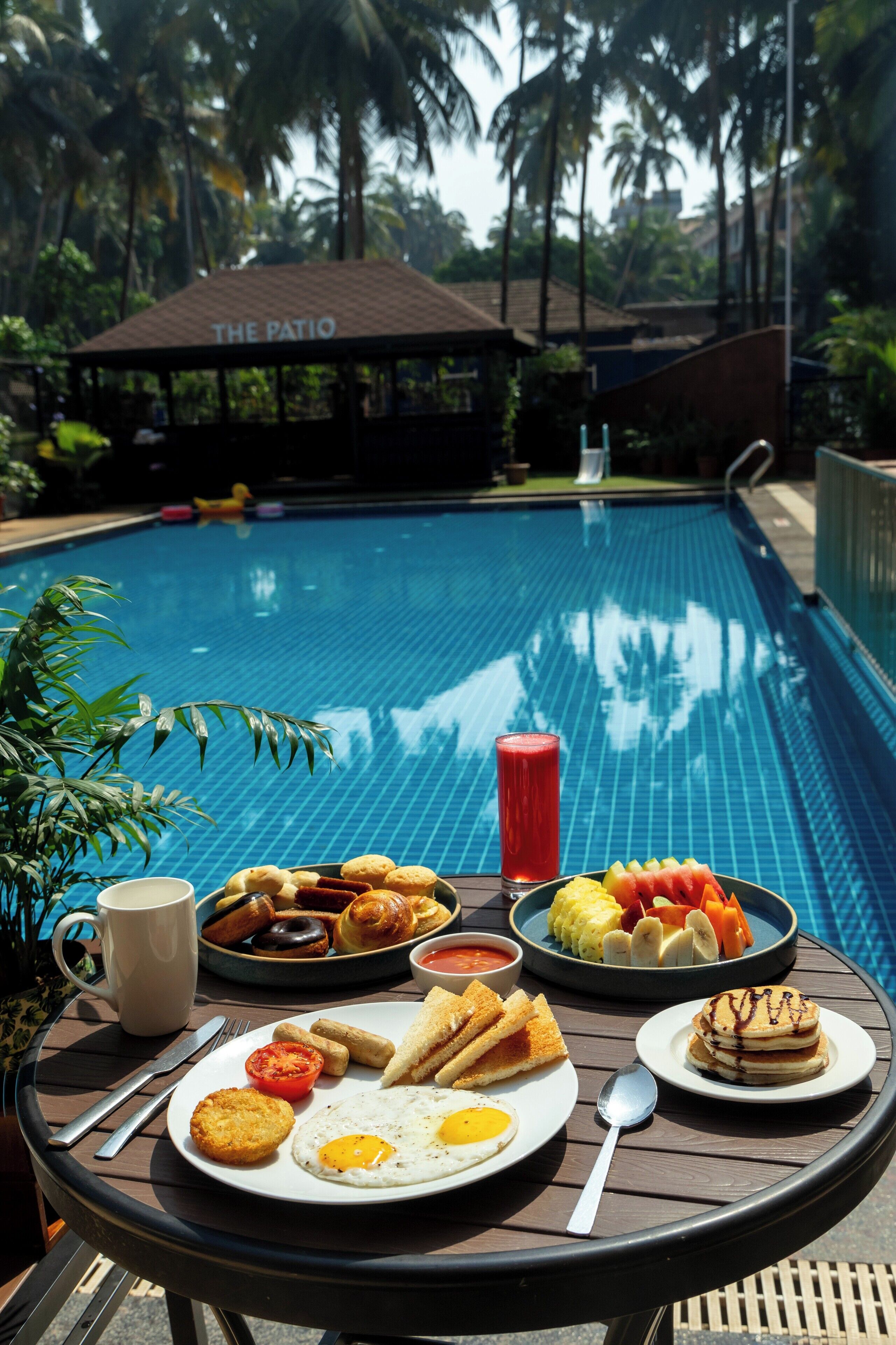 A dining table with breakfast items by a poolside, including eggs, toast, and fruit.