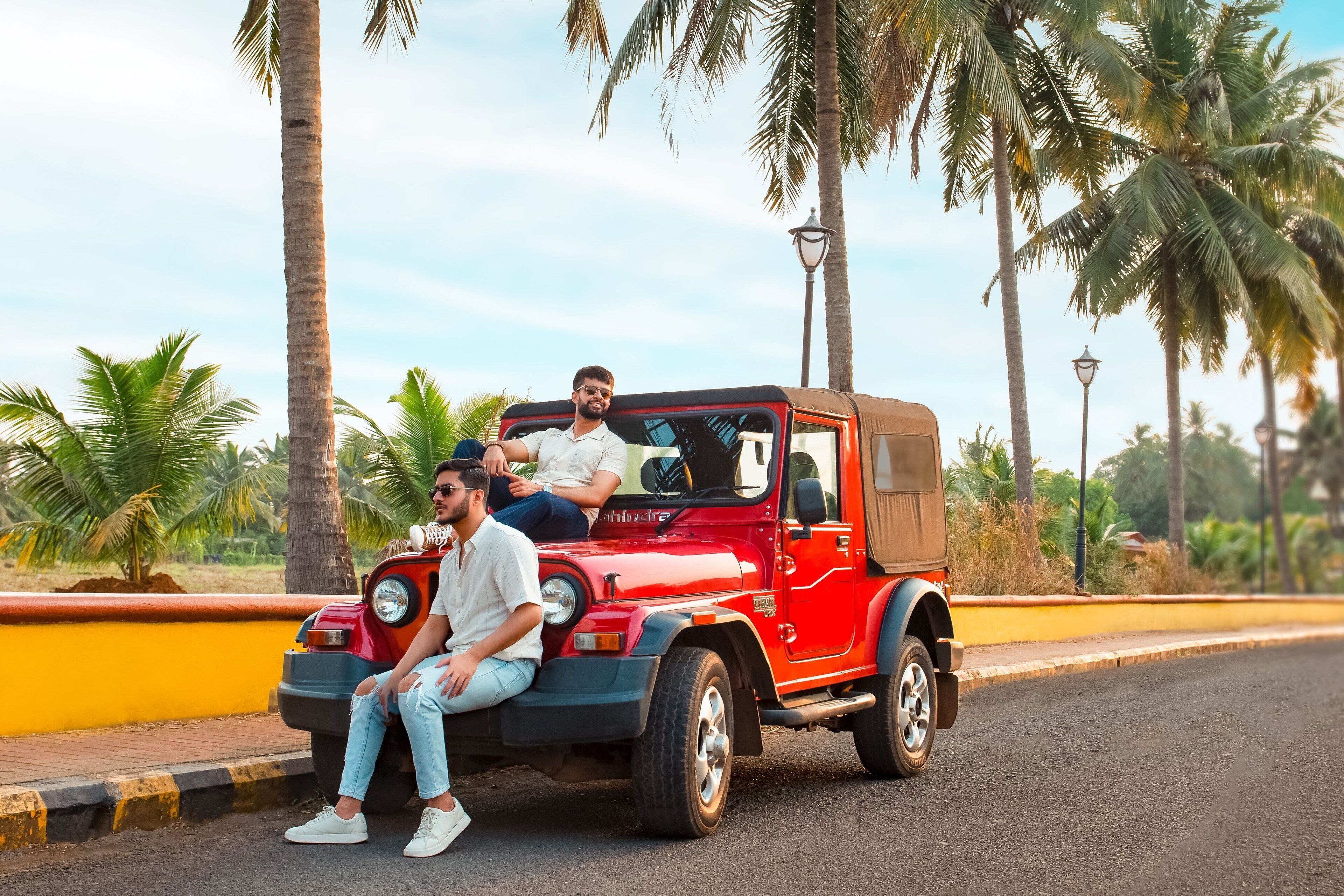 Ein roter Jeep mit zwei Personen, abgestellt auf einer Straße mit Palmen und einem gelben Bordstein.